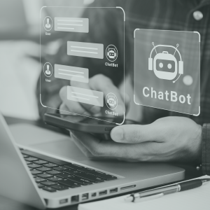 Muvraline_ChatBot_IA Vue rapprochée d'une main tenant un téléphone devant un ordinateur avec une illustration d'une conversation entre une personne et un ChatBot