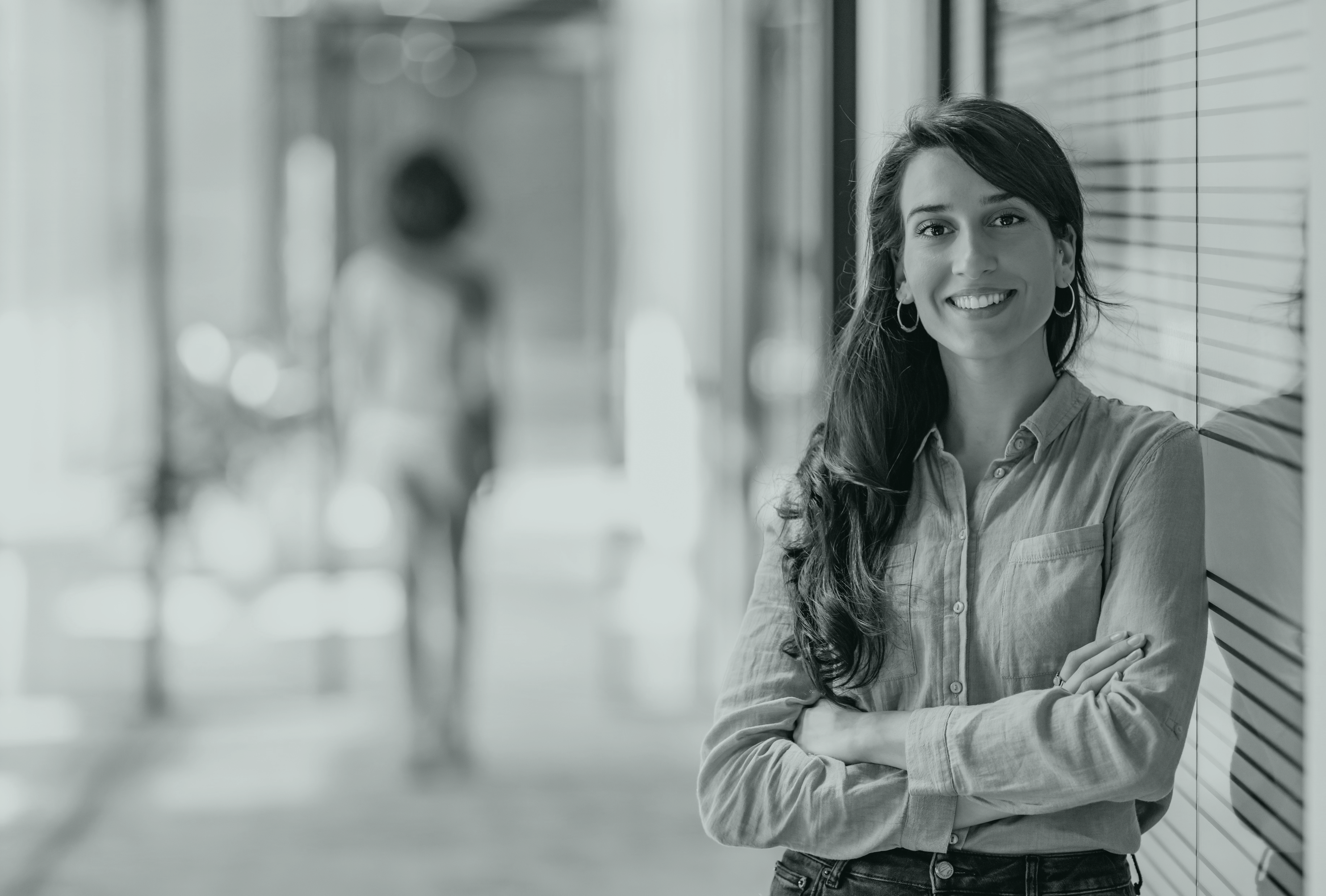 Mujer sonriente en un pasillo, con el hombro apoyado en la pared de cristal de una habitación