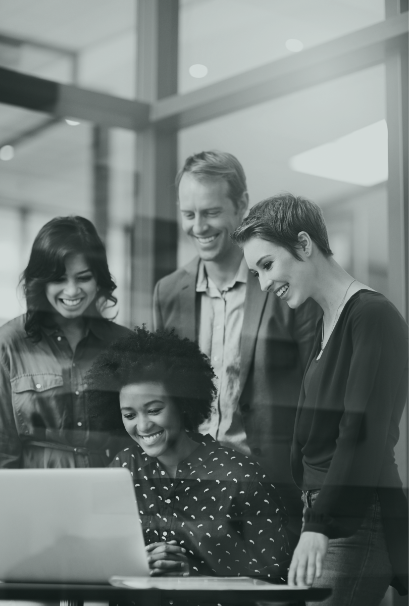 A group of smiling people gathered around a computer in an office