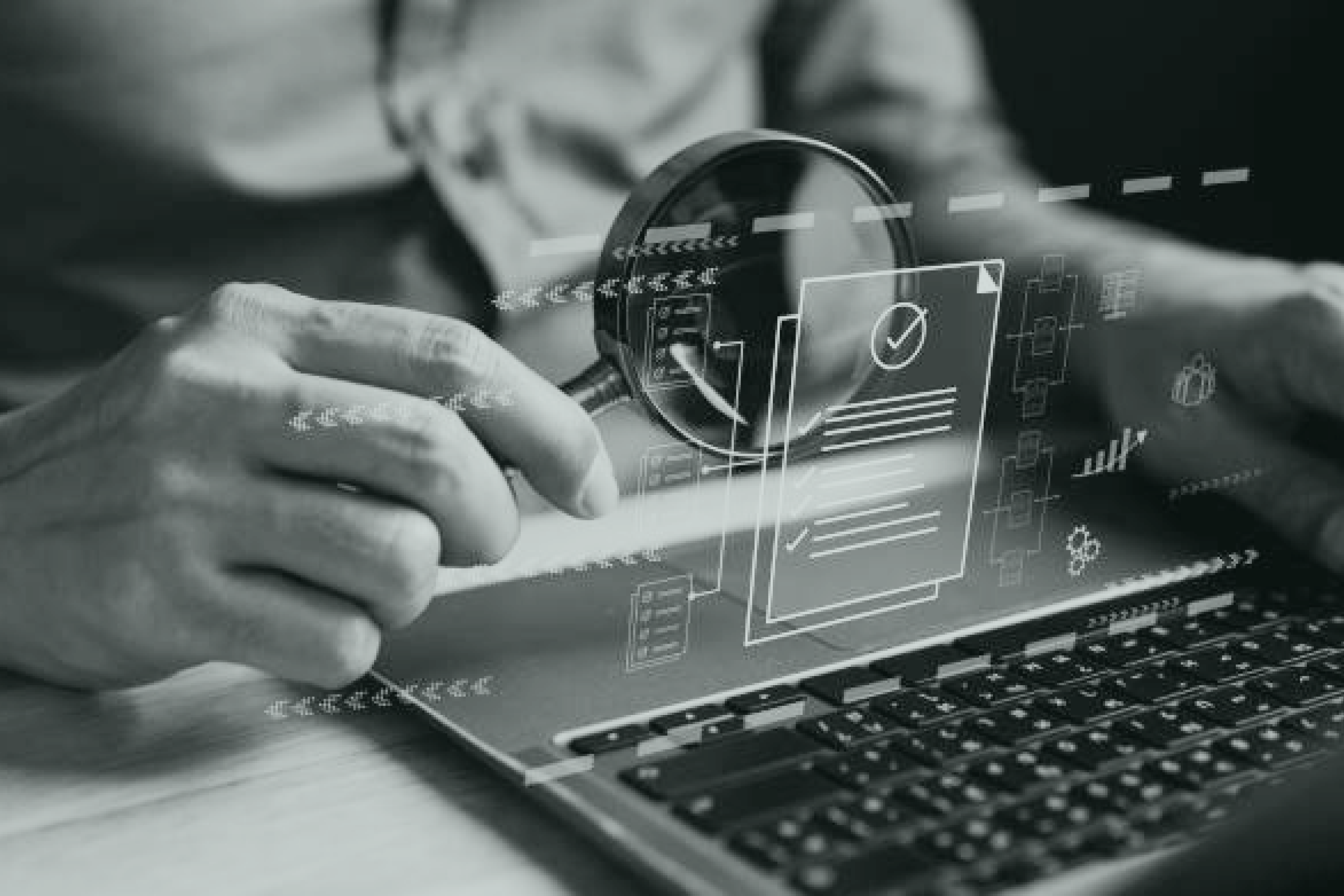 Close-up of a hand holding a magnifying glass in front of a computer with illustrations of documents, cogs and curves