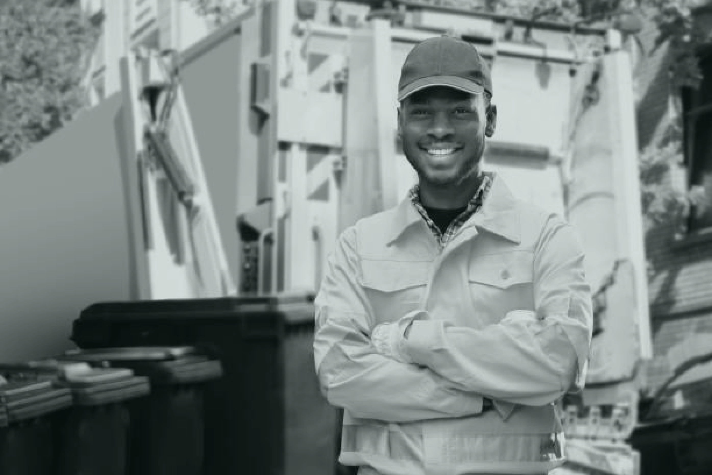 Employé municipal souriant devant un camion de ramassage d'ordures et des poubelles de recyclage