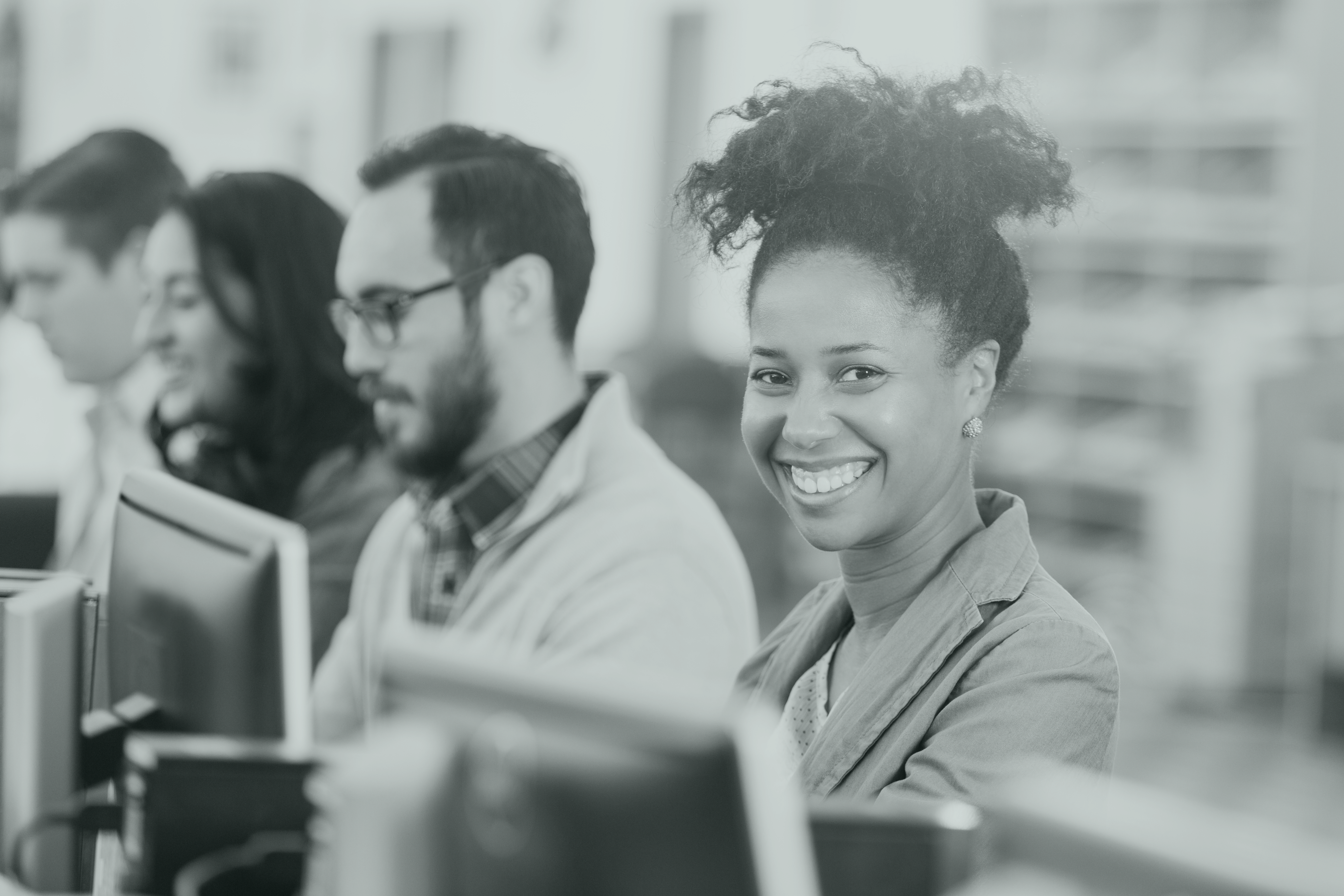 Groupe de personnes travaillant sur leur ordinateur, trois d'entre elles ayant la tête penchée, la dernière souriant en direction de l'objectif